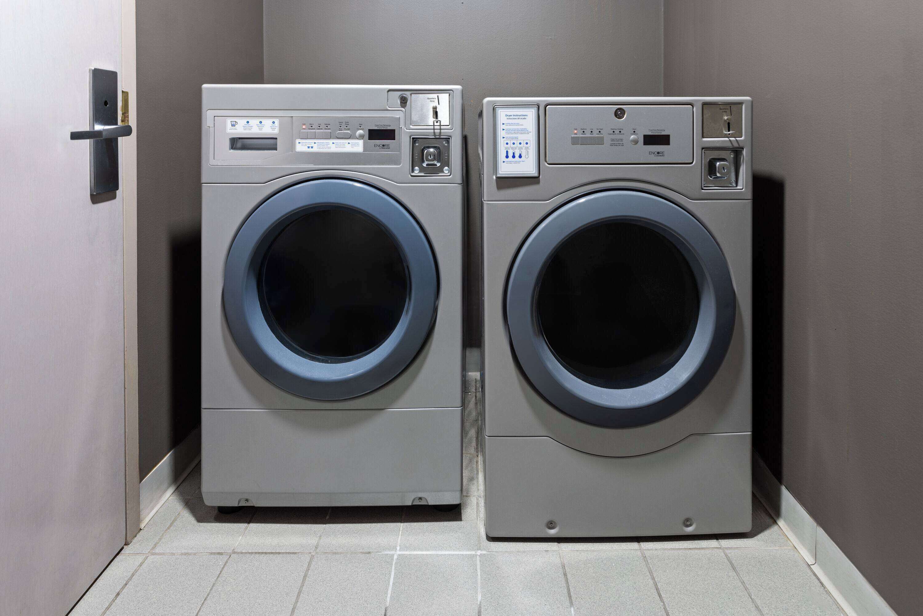 Two front-loading washing machines in a laundry room with a door on the left.
