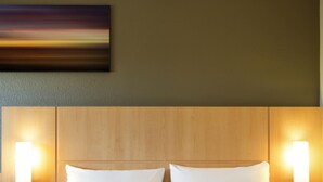 Une chambre d’hôtel avec une tête de lit en bois, deux oreillers blancs et des lampes fixées au mur.