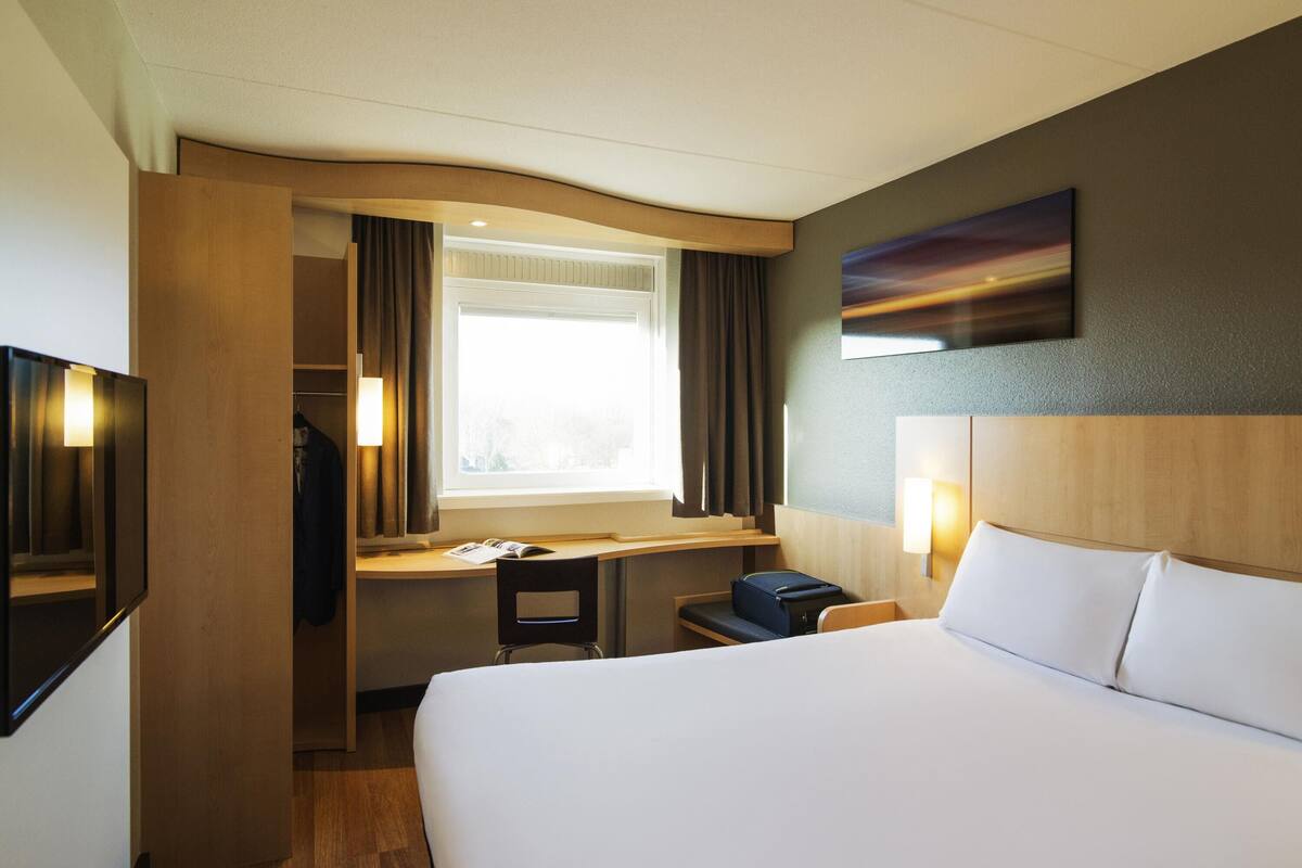 Hotellihuone, jossa on sänky, työpöytä, tuoli ja televisio.