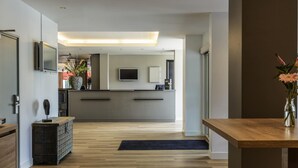 Un hall d’hôtel moderne avec un plancher en bois, un comptoir d’accueil, un téléviseur et un grand miroir.