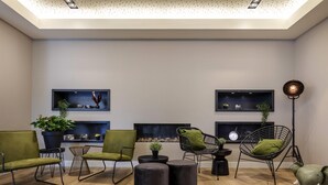 Un salon moderne avec un plancher en bois, des fauteuils verts et noirs, un pouf noir rond et un lampadaire noir.