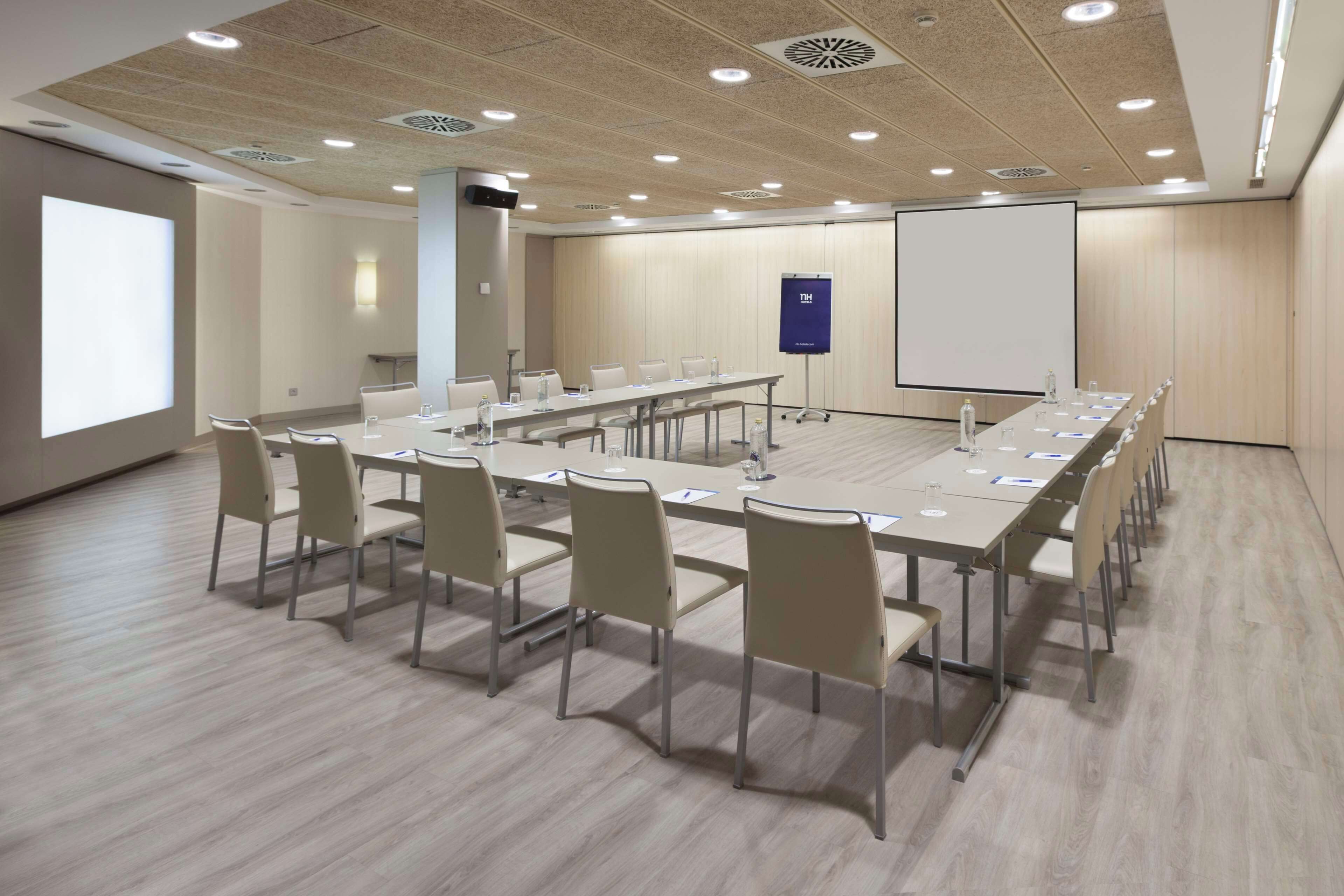Una sala de conferencias con una larga mesa, sillas, una pantalla de proyector y una pizarra.