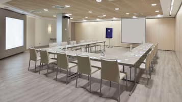 Una sala de conferencias con una larga mesa, sillas, una pantalla de proyector y una pizarra.