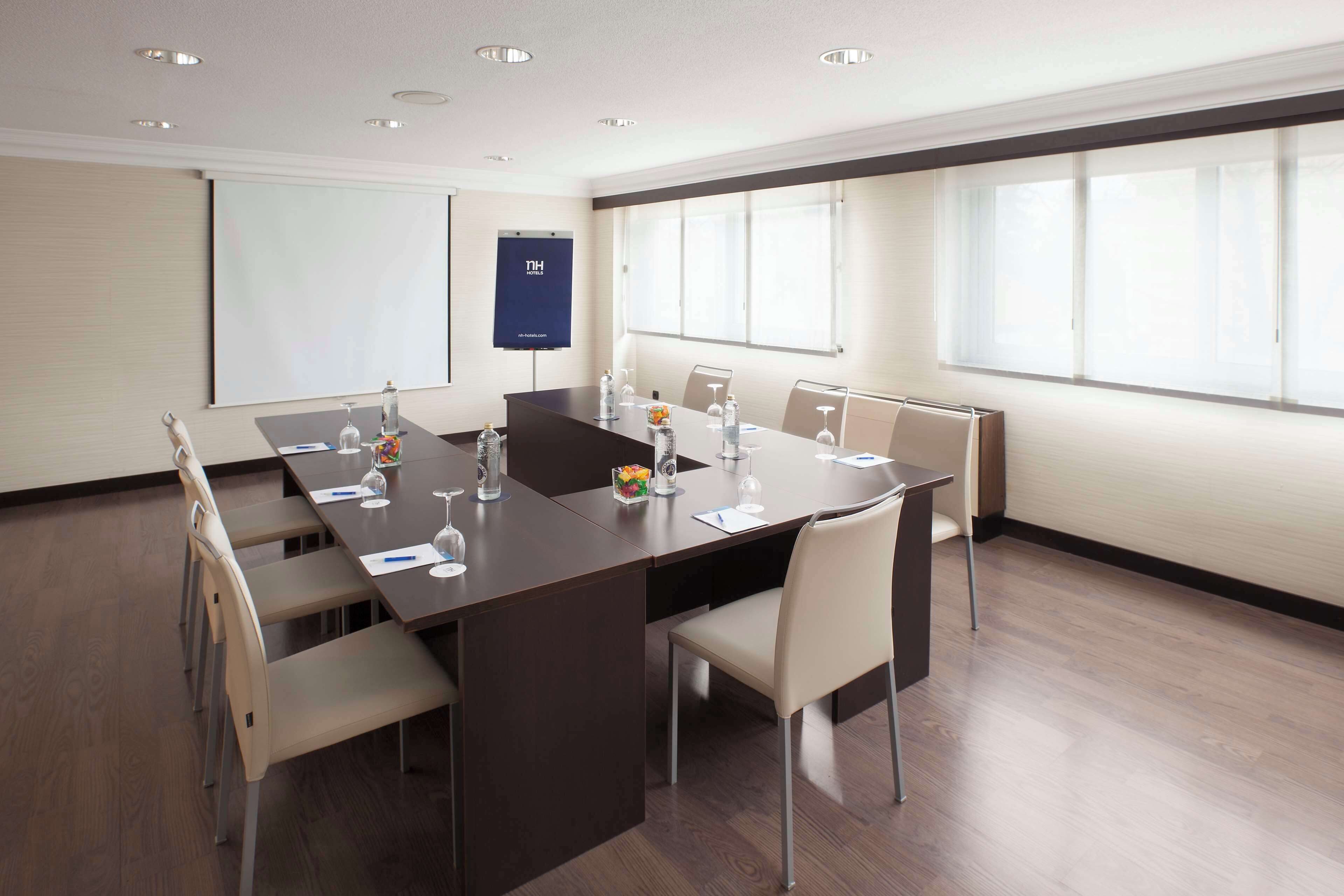 A conference room with a long table, chairs, a projector screen, and a window.