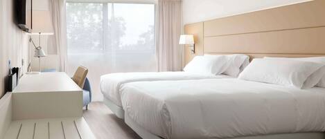 Habitación de hotel con una cama grande, un escritorio, un televisor y una ventana con cortinas.