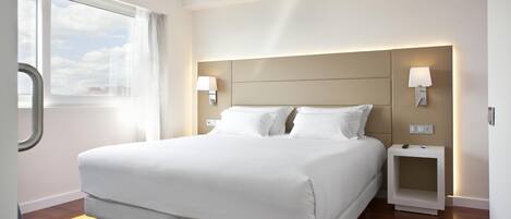 Una habitación de hotel moderna con una cama grande, dos mesitas de noche con lámparas, una ventana con cortinas y suelo de madera.