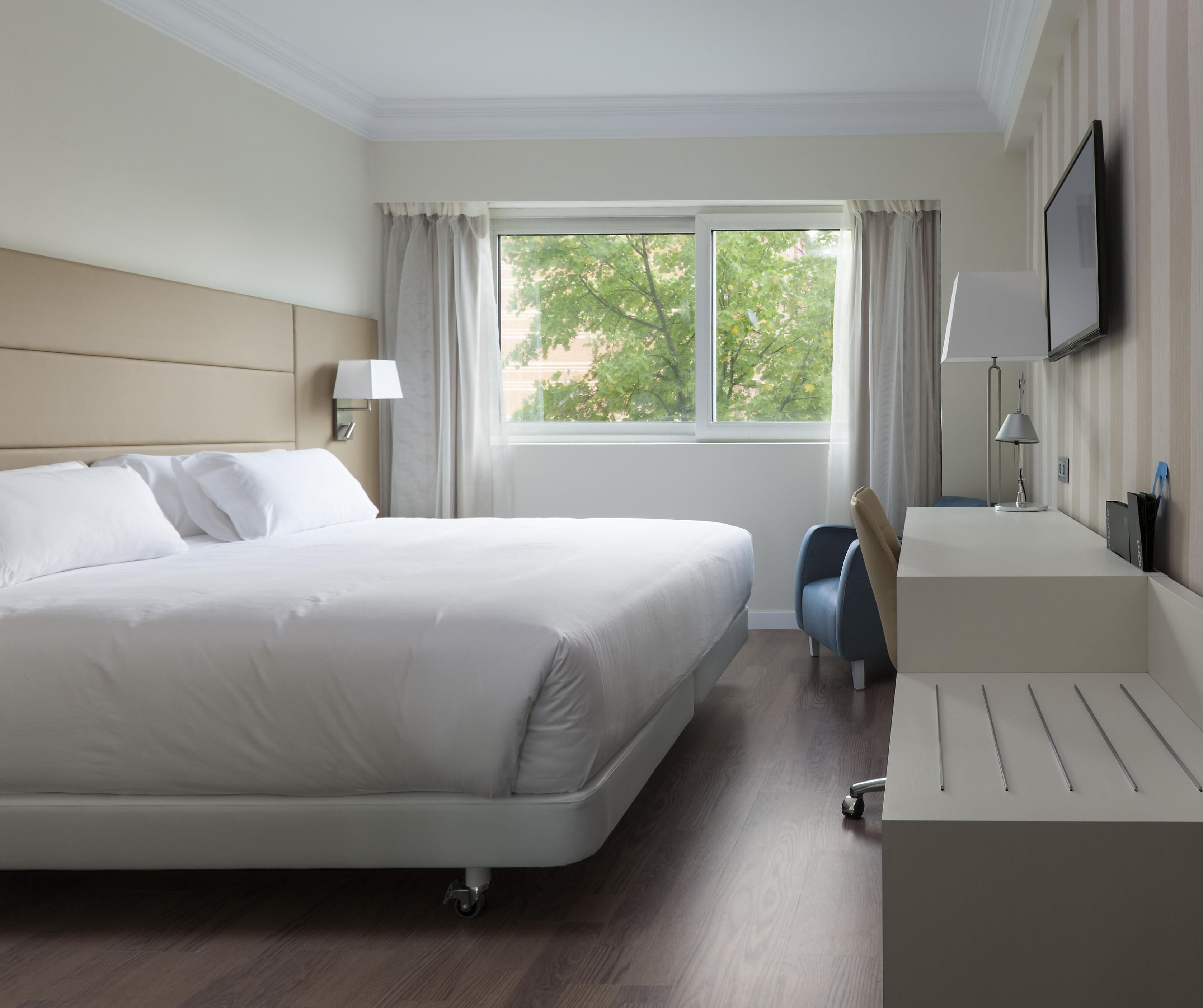 Een hotelkamer met een groot bed, een bureau, een stoel, een televisie en een raam met gordijnen.