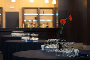 A bar area with multiple tables, each with a glass set and a vase with a single flower. - NH Pamplona Iruña Park (Pamplona)