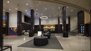 A spacious lobby with high ceilings, polished granite floors, and a central area with round tables. - NH Pamplona Iruña Park (Pamplona)