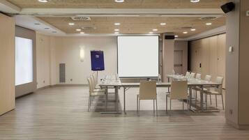 A conference room with a large table, chairs, a projector screen, and a presentation screen.