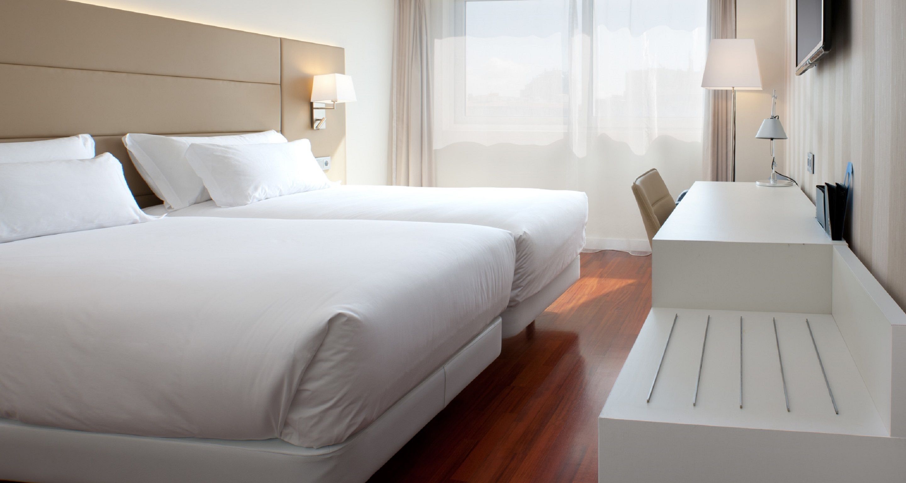 A hotel room with two beds, a desk, a chair, and a TV mounted on the wall.