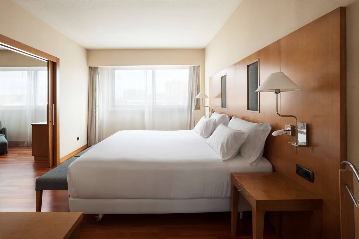Une chambre d’hôtel avec un grand lit, une table de chevet et une vue sur la ville par la fenêtre.