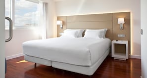 A modern hotel room with a large bed, two bedside tables, and a view of the sky through the window. - NH Pamplona Iruña Park (Pamplona)