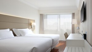 A hotel room with two beds, a desk, a chair, a TV, and a window with curtains. - NH Pamplona Iruña Park (Pamplona)