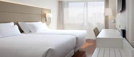 A hotel room with two beds, a desk, a chair, a TV, and a window with curtains.