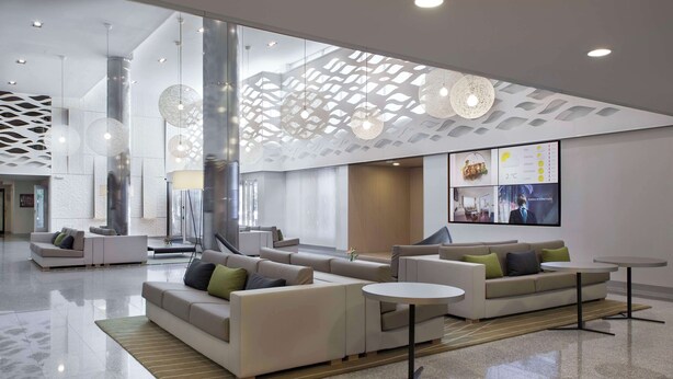 A modern lobby with a large seating area, a reception desk, and a digital display. - NH Pamplona Iruña Park (Pamplona)
