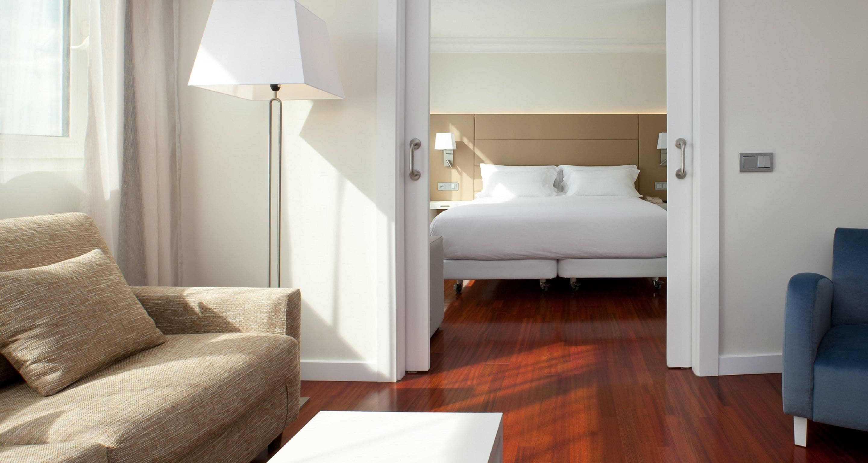A hotel room with a bed, a sofa, a lamp, and a chair.