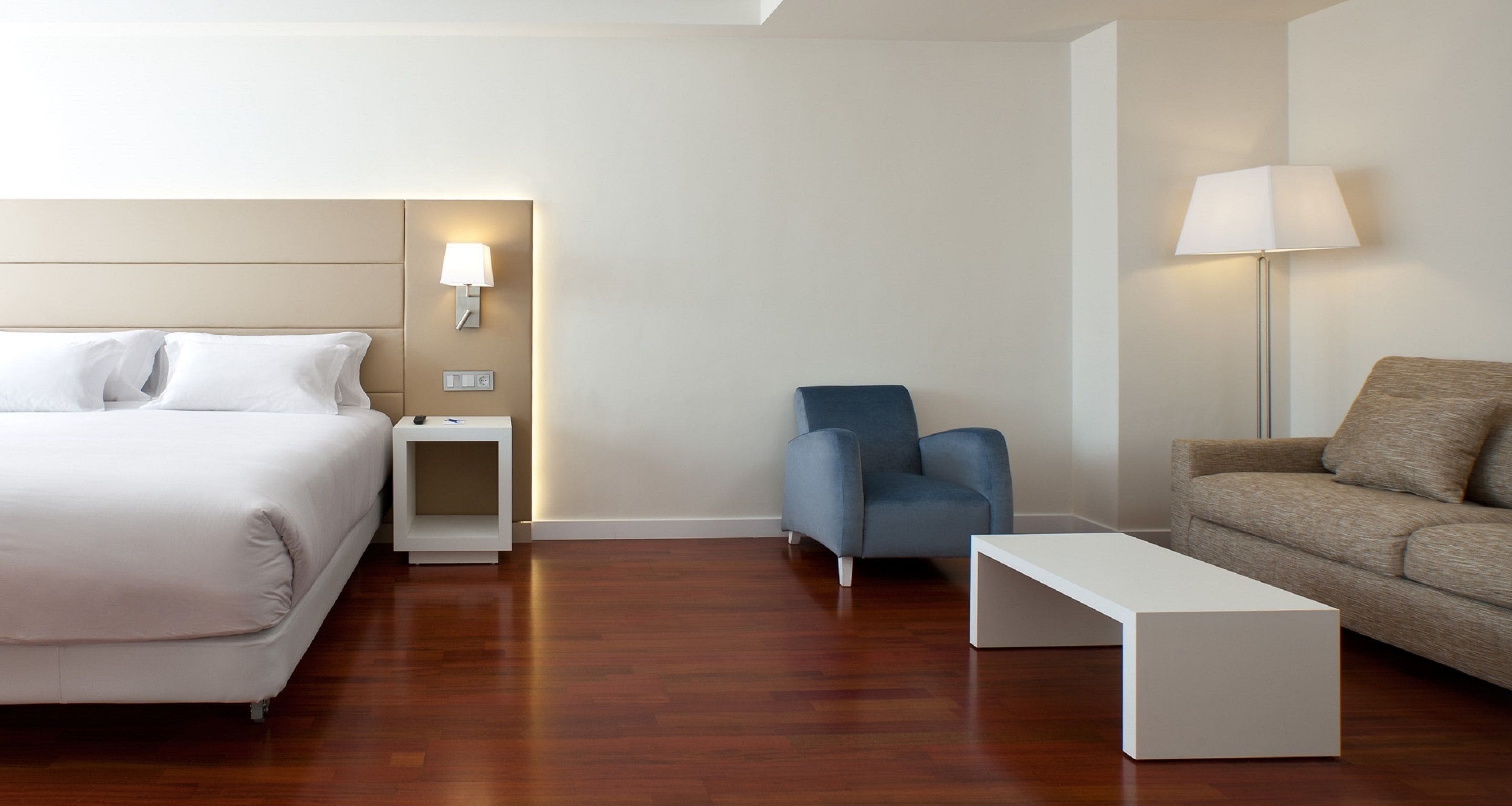 A hotel room with a bed, a desk, a chair, a sofa, and a lamp.