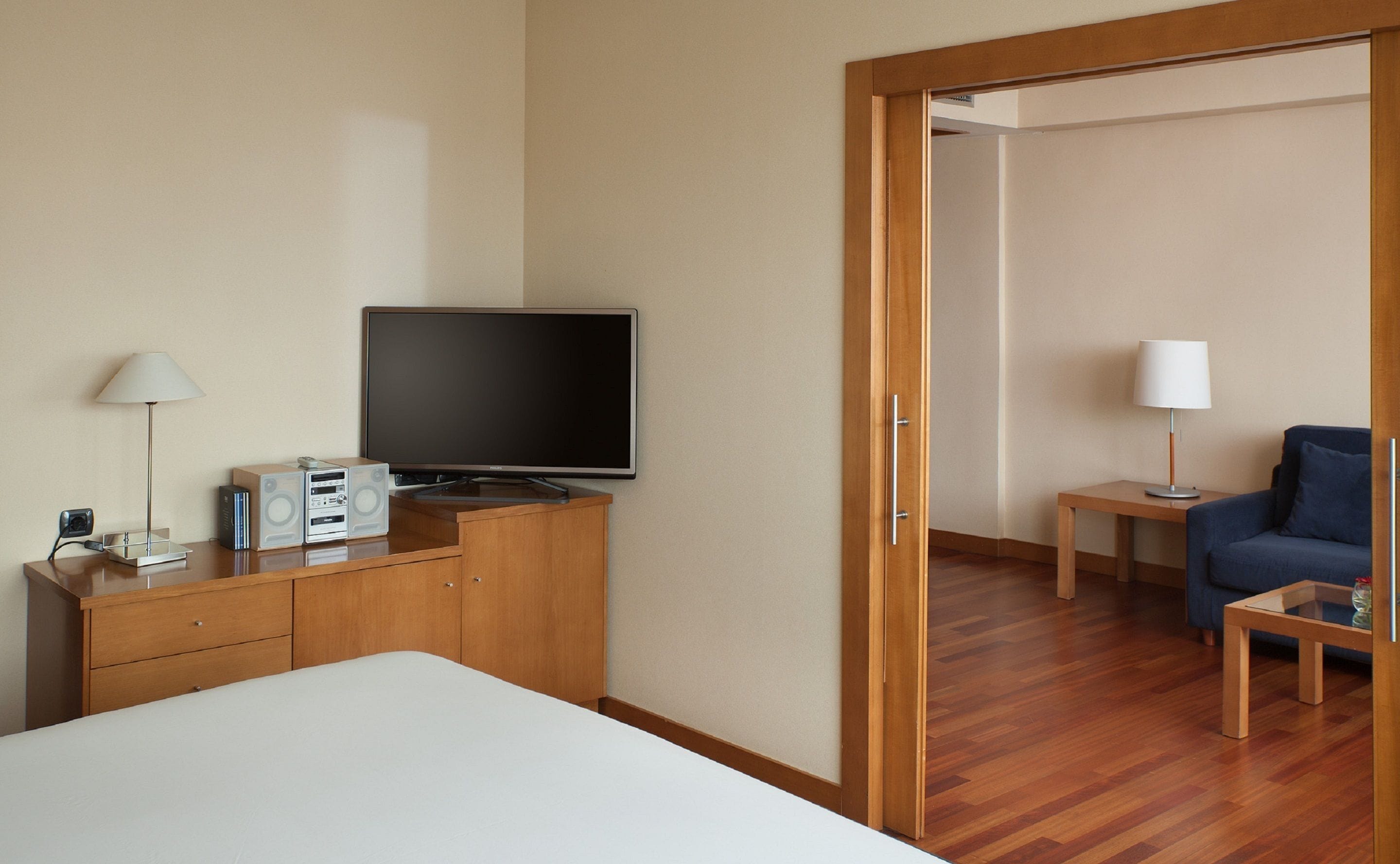 A hotel room with a bed, a TV, a desk with a computer, a chair, and a lamp.