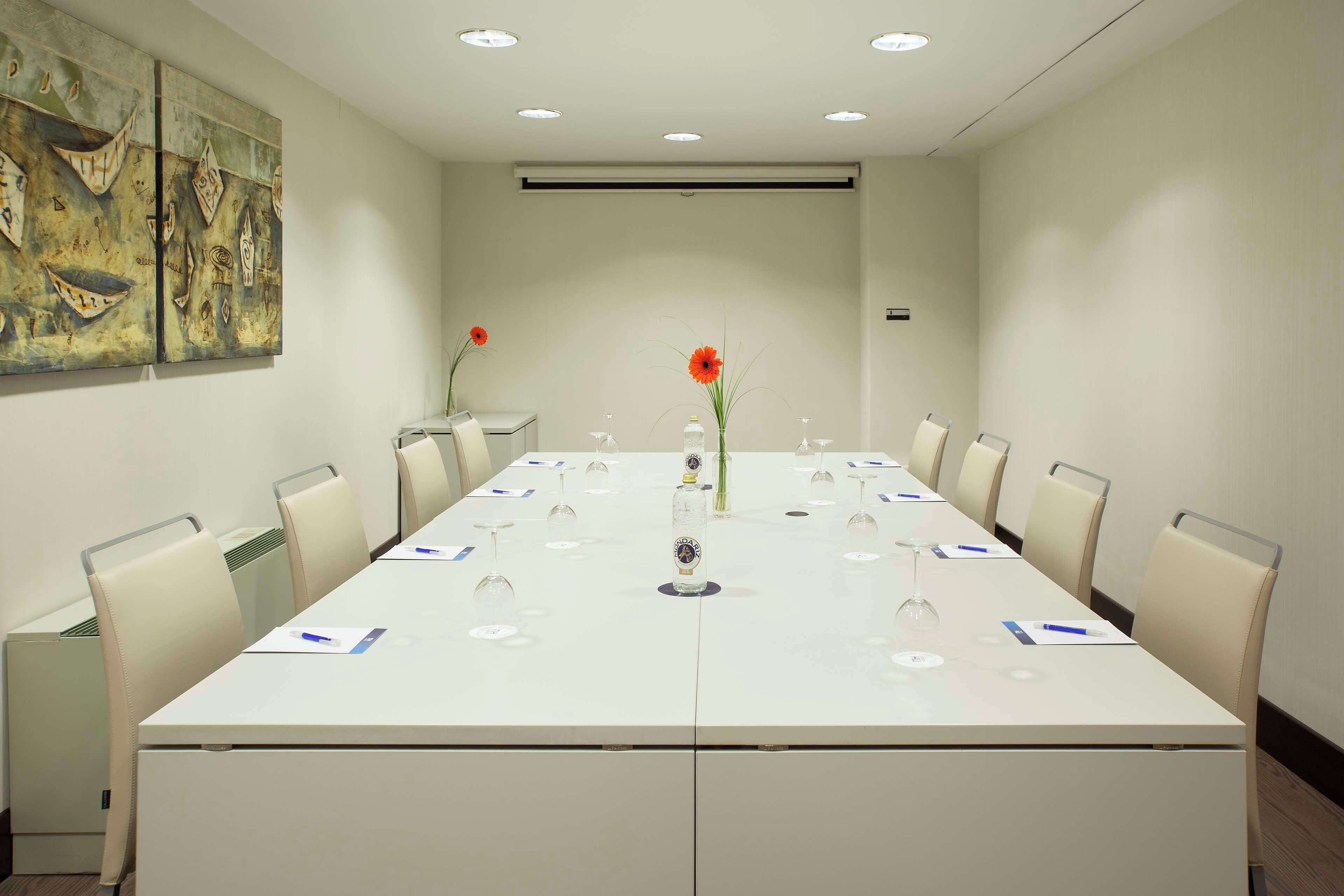 Un salón de conferencias con una larga mesa, sillas y un jarrón con flores.