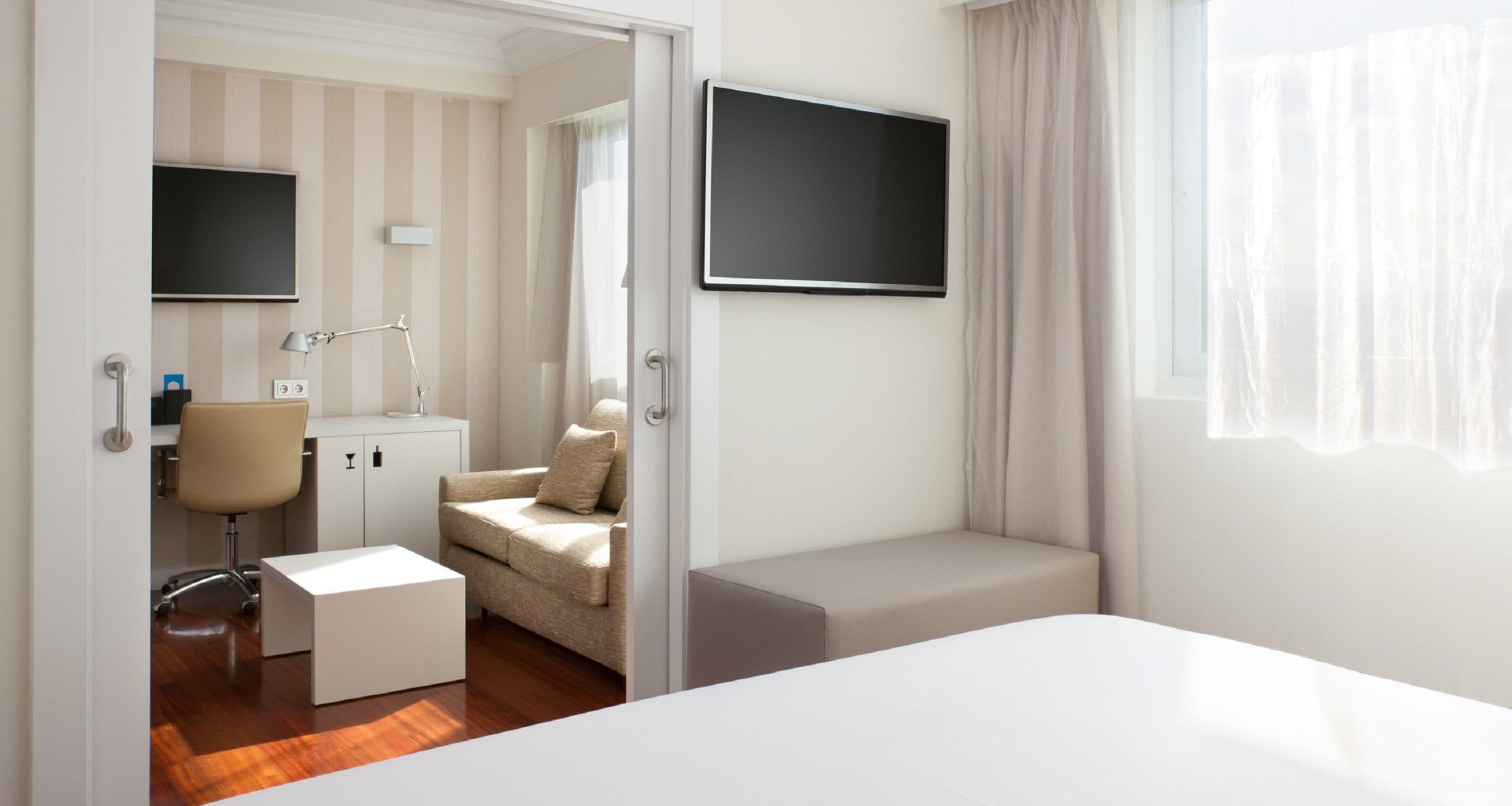 A modern hotel room with a bed, a desk, a chair, a sofa, and a TV.