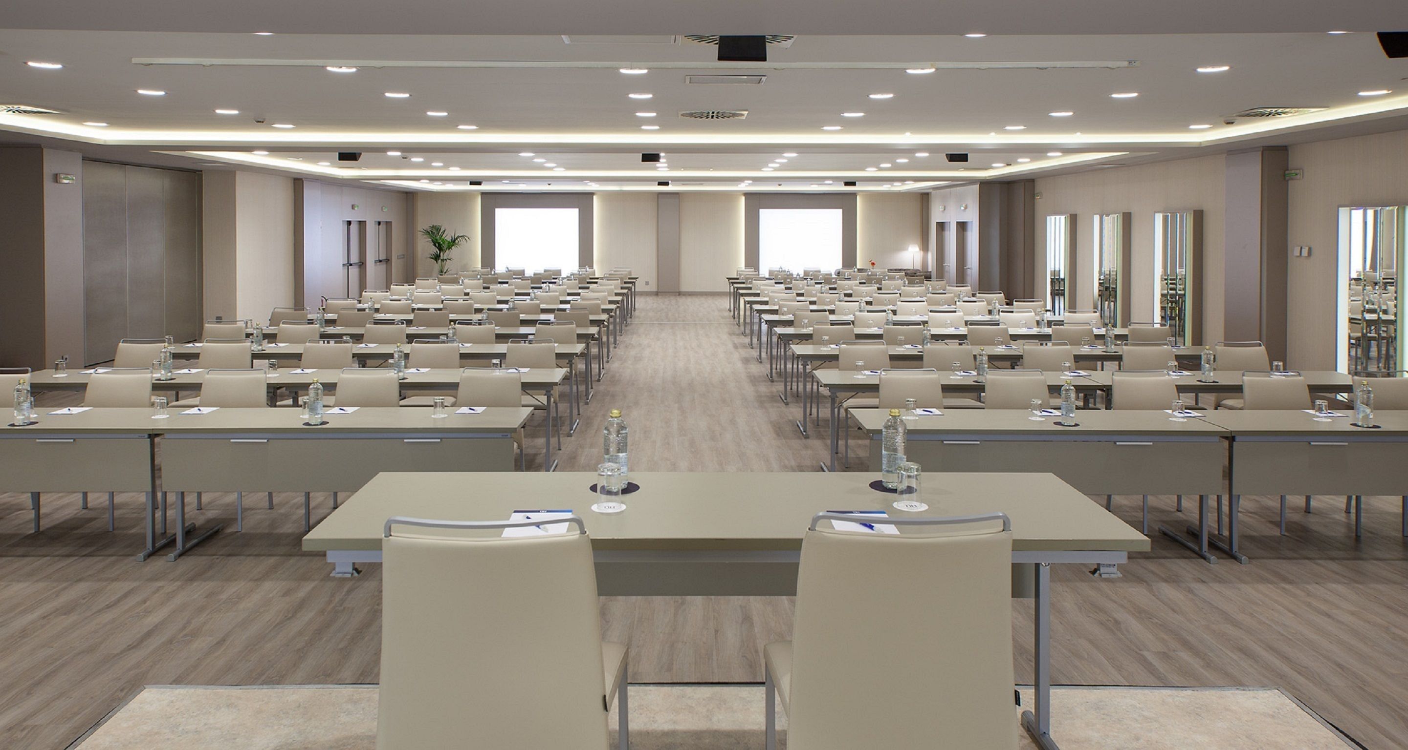 A large conference room with rows of tables and chairs, equipped with water bottles and nameplates.
