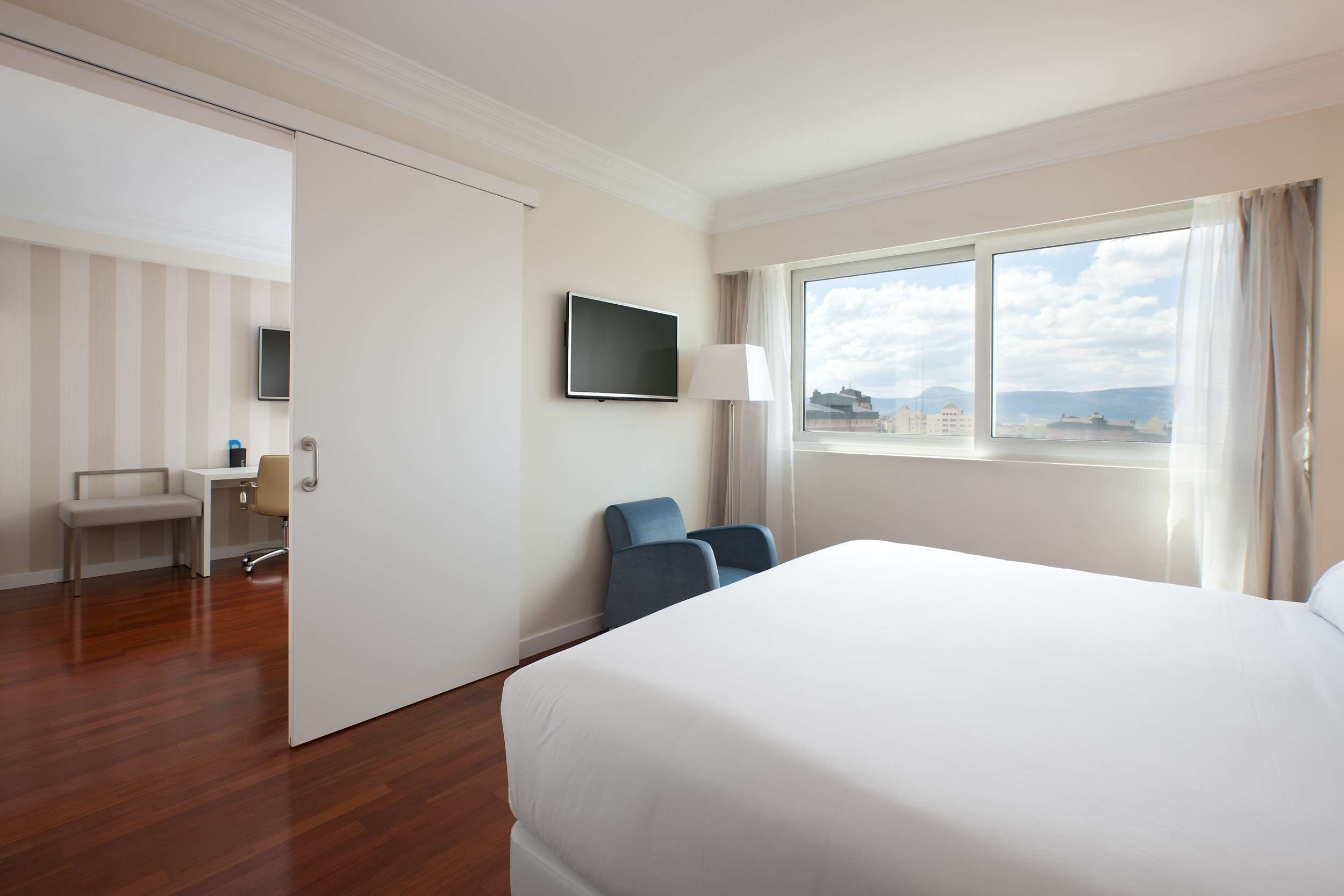 A hotel room with a large bed, a desk with a chair, a TV, and a window with a view.