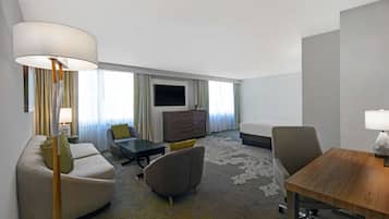 A modern hotel room with a sofa, armchairs, a small table, a TV, and a bed.