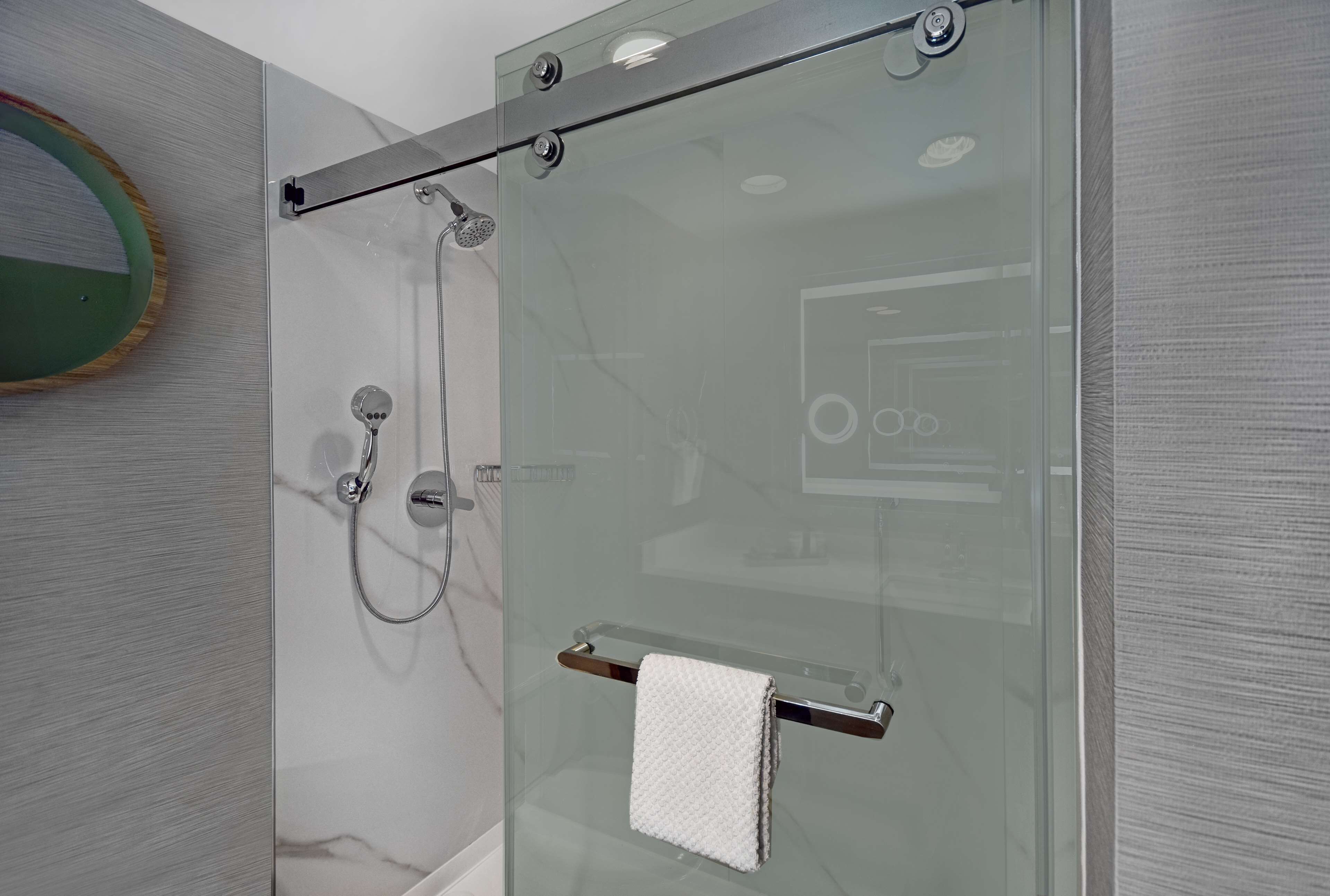 A modern bathroom with a glass shower enclosure, a towel rack, and a marble wall.