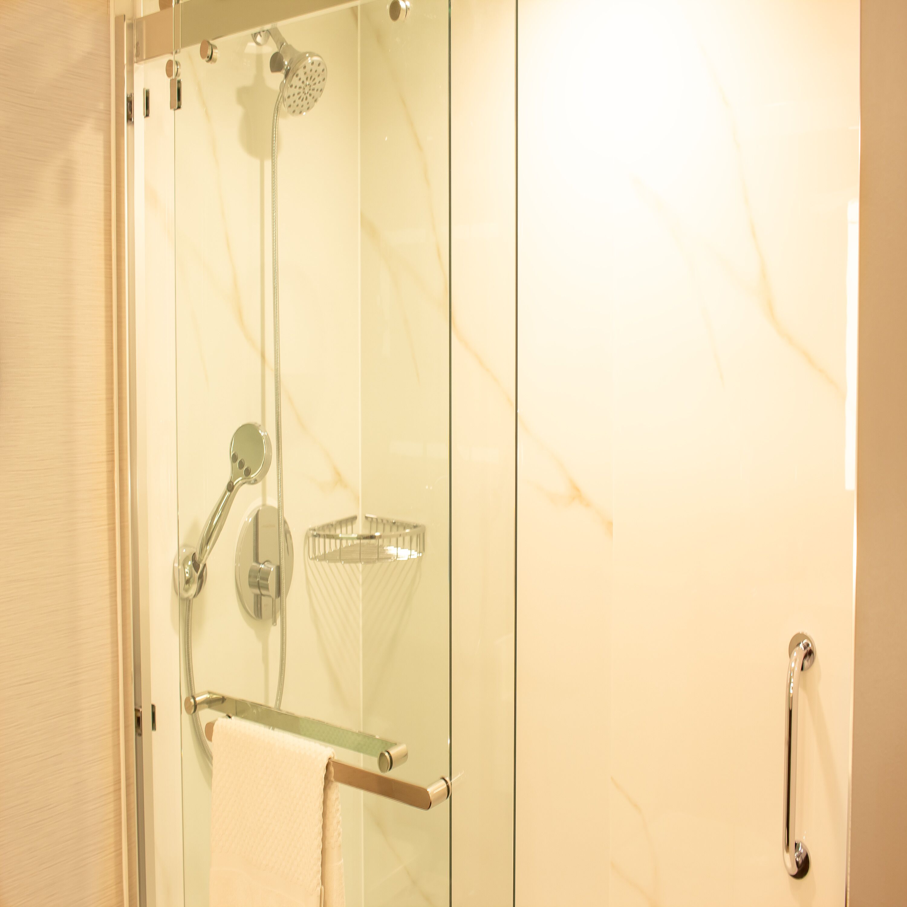 A glass-enclosed shower with a handheld showerhead, a glass shelf, and a towel rack.