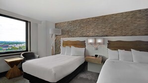 Ein Hotelzimmer mit einem großen Bett, einem Nachttisch, einem Sessel und Blick auf die Stadt durch ein großes Fenster.
