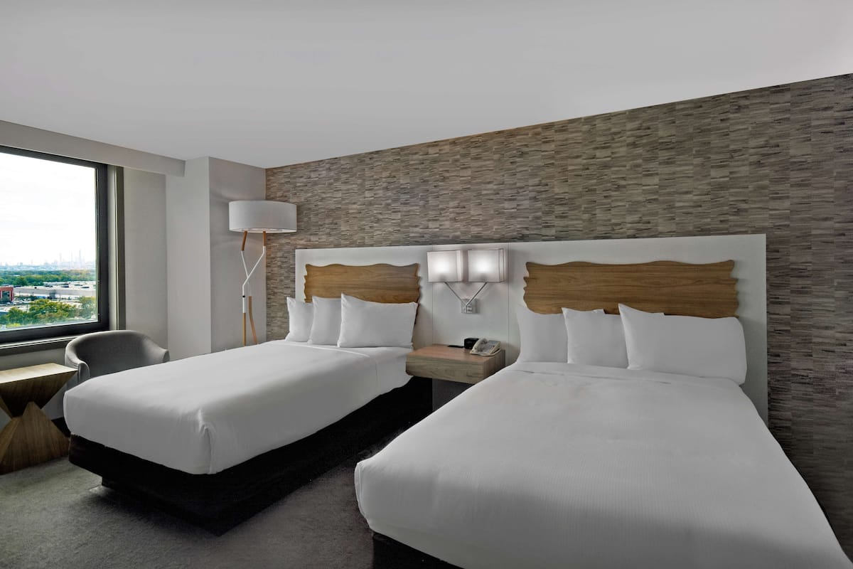 Een hotelkamer met twee bedden, een bureau, een stoel, een lamp en uitzicht op de stad.