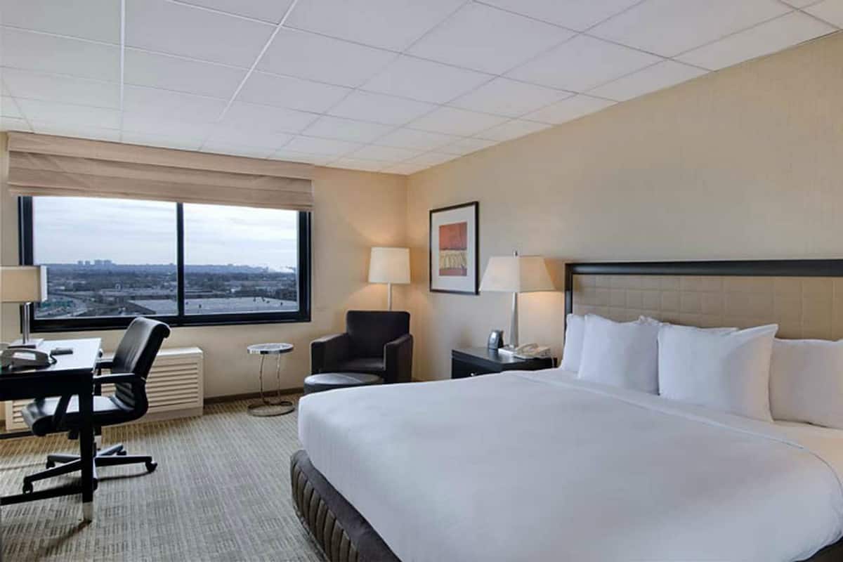 Een hotelkamer met een groot bed, een bureau met stoel, een klein tafeltje, twee lampen en een raam met uitzicht op de stad.