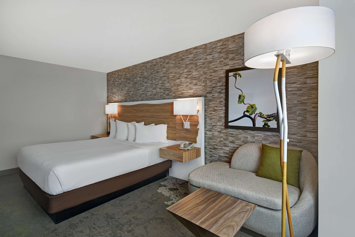 Een moderne hotelkamer met een groot bed, een nachtkastje met lamp, een bank en een kleine houten tafel.