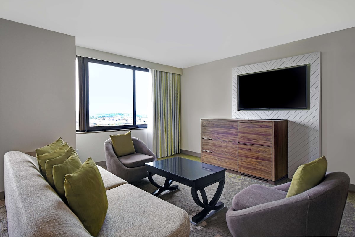 Een moderne hotelkamer met een bank, fauteuils, een salontafel, een aan de muur bevestigde televisie en een houten kast.
