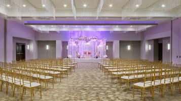 A large hall with rows of chairs facing a stage with floral decorations and a podium.