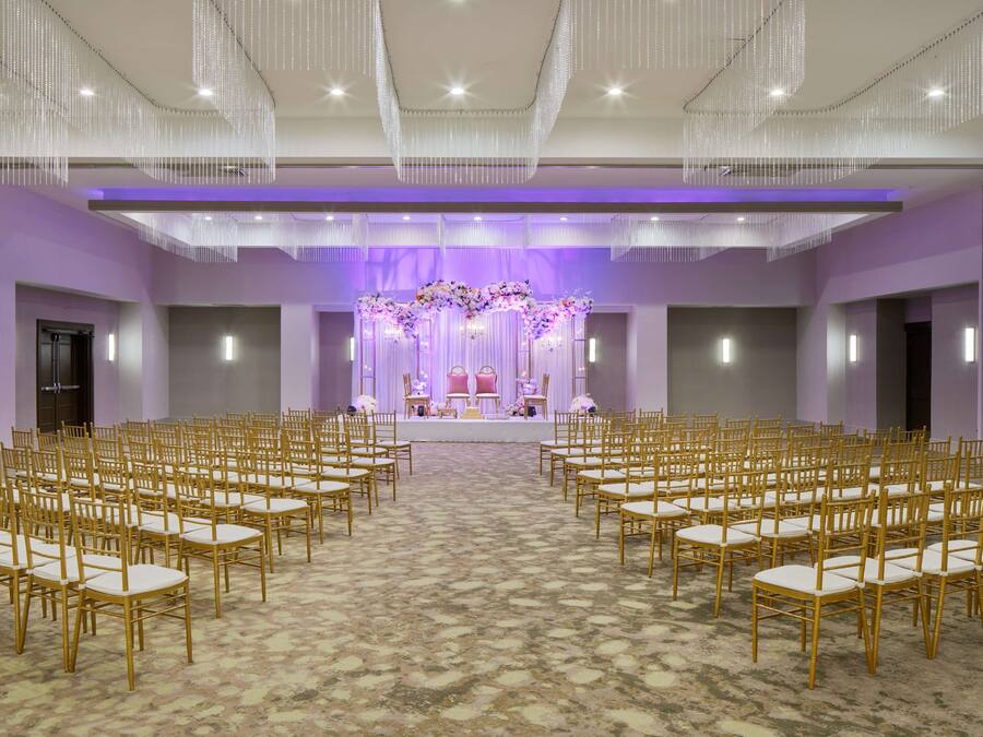 A large hall with rows of chairs facing a stage with floral decorations and a podium.