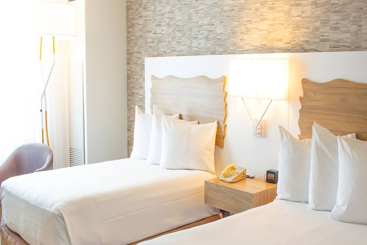 Een hotelkamer met twee bedden, een nachtkastje met telefoon en wekker, een stoel, en een stenen muur.