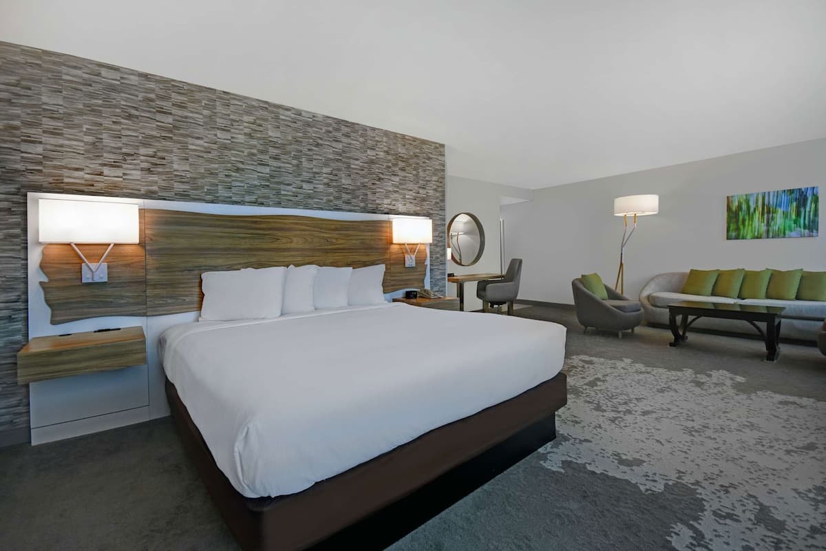 Een moderne hotelkamer met een groot bed, een houten hoofdeinde, een nachtkastje, een bureau, een stoel, een bank en een schilderij aan de muur.