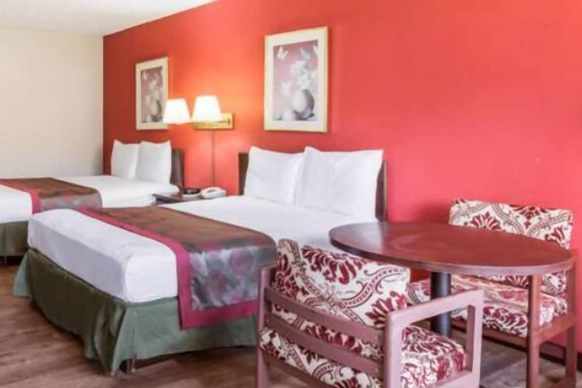 A hotel room with two beds, a desk, a chair, and a table.