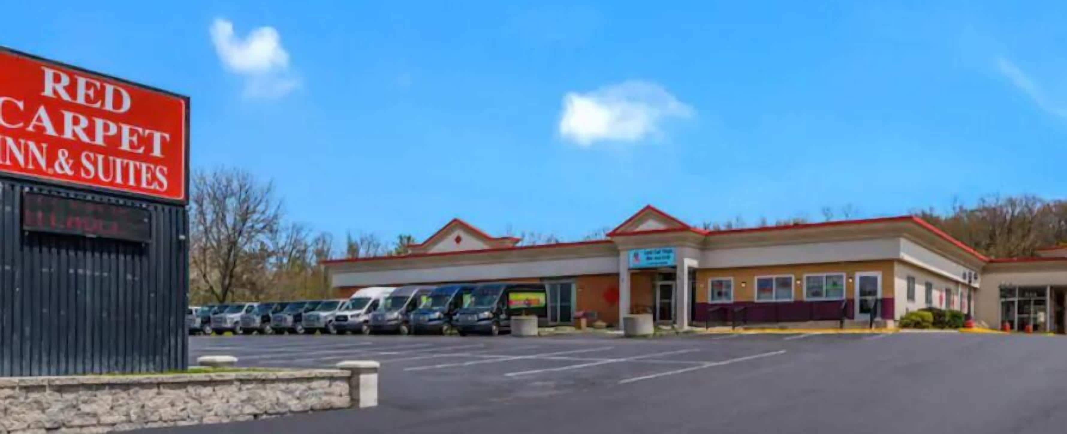Un hôtel Red Carpet Inn & Suites doté d’un parking où plusieurs voitures sont garées devant l’entrée.