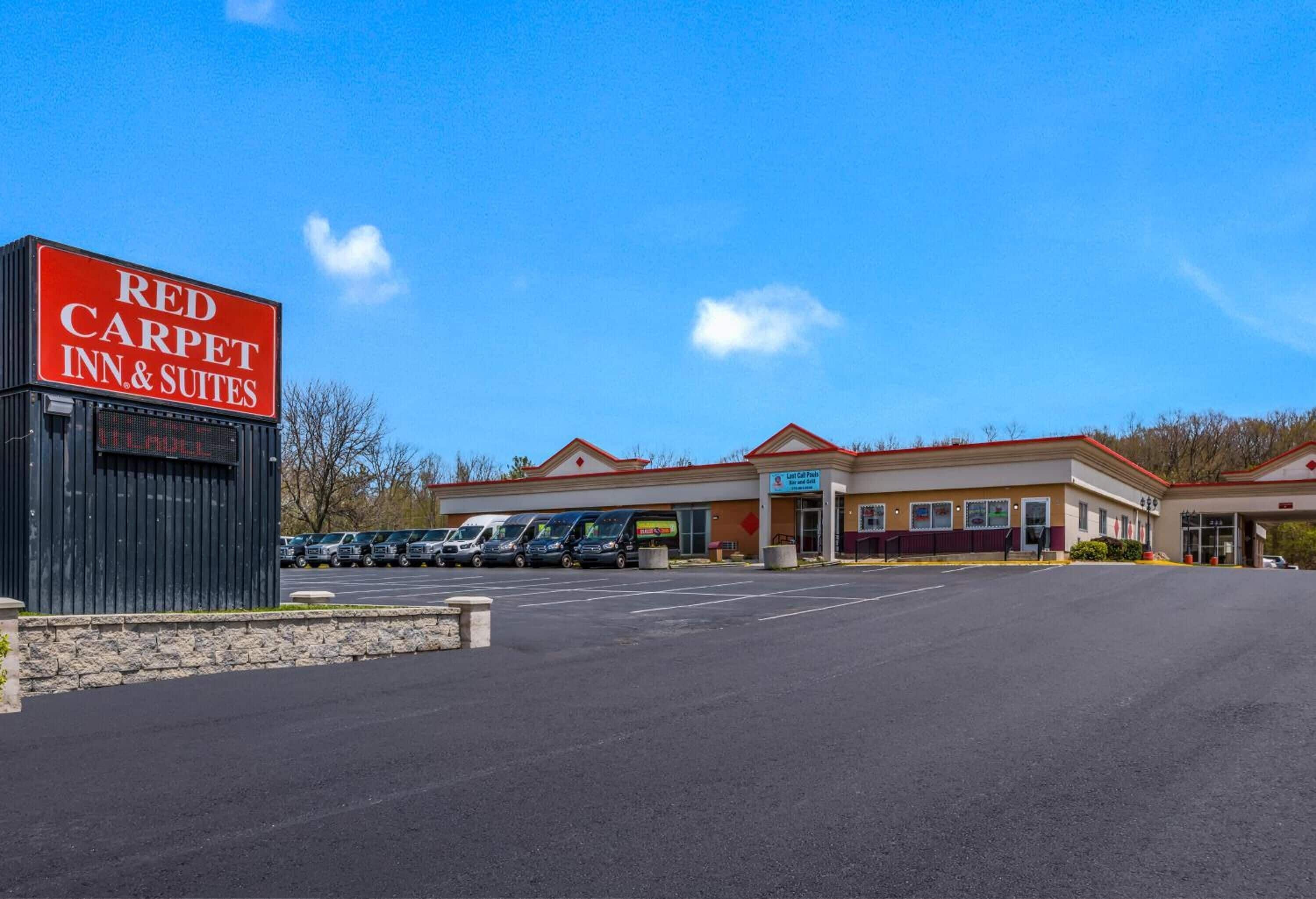 A Red Carpet Inn & Suites with a clear sky, a parking lot, and a building with a red roof.