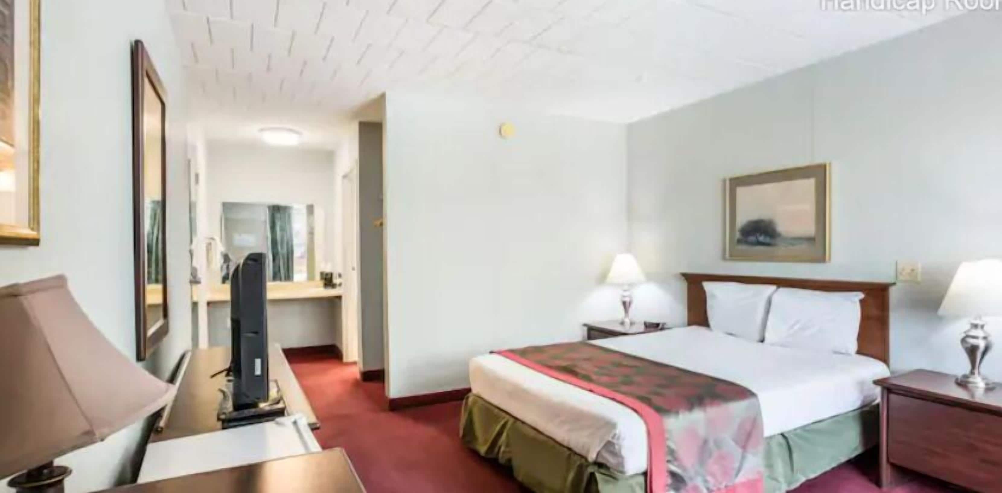A hotel room with a bed, bedside tables, a desk, a chair, a mirror, and a door leading to another room.
