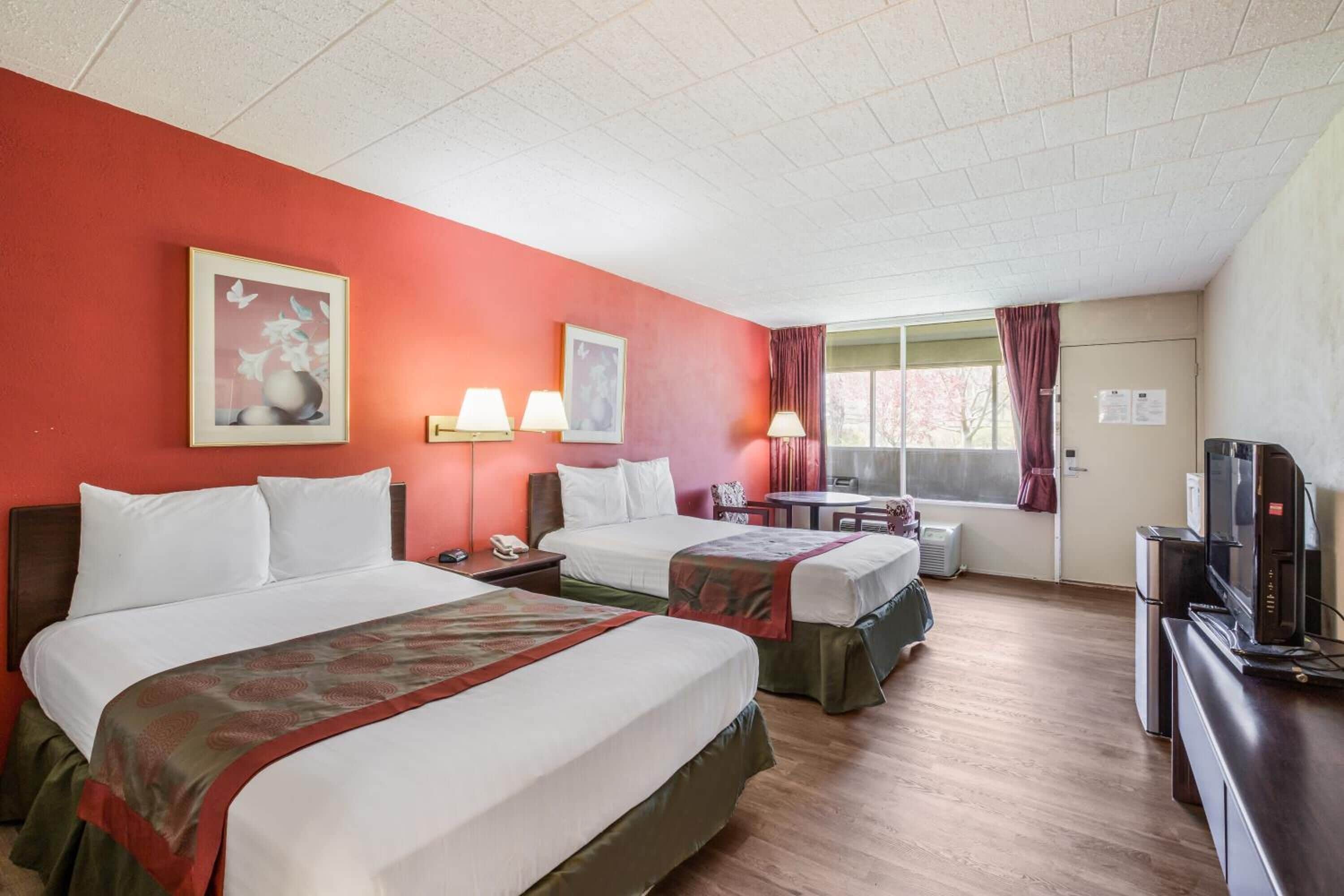 A hotel room with two beds, a television, a desk, and a window with curtains.