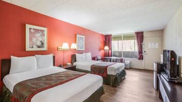 A hotel room with two beds, a television, a desk, and a window with curtains.