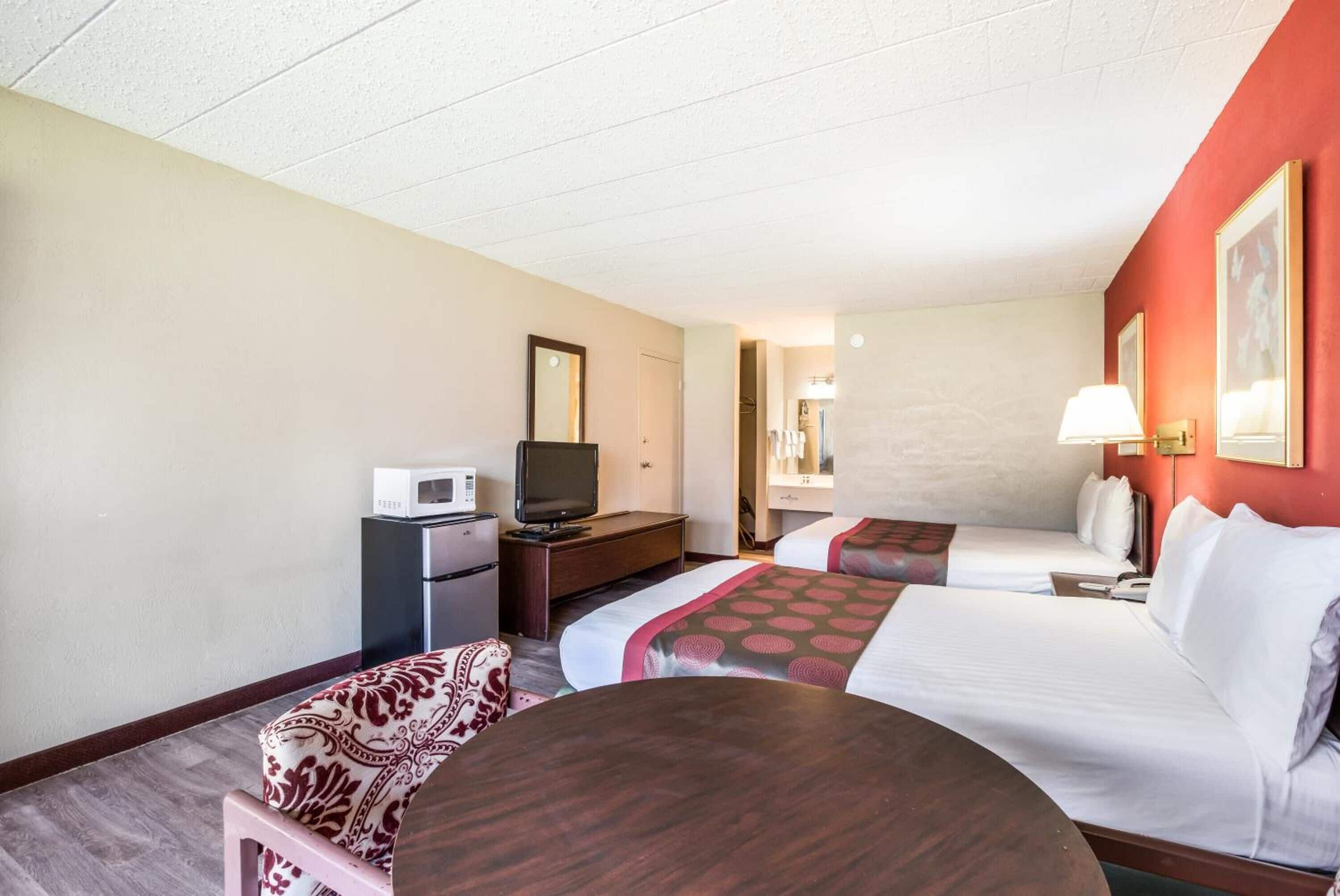 A hotel room with two beds, a desk with a TV, a microwave, and a small seating area.
