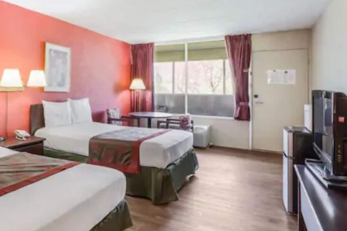 A hotel room with two beds, a desk, a chair, a television, and a window with curtains.