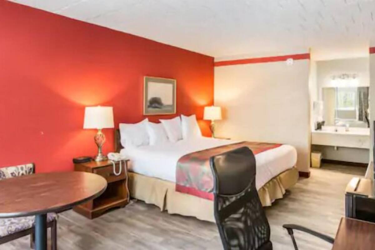A hotel room with a bed, two bedside tables, a desk with a chair, a round table, and a mirror.