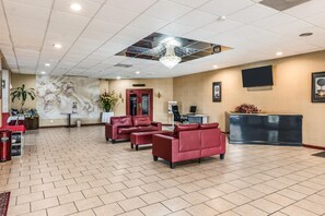 A lobby with a reception desk, red leather sofas, a chandelier, and a tiled floor.