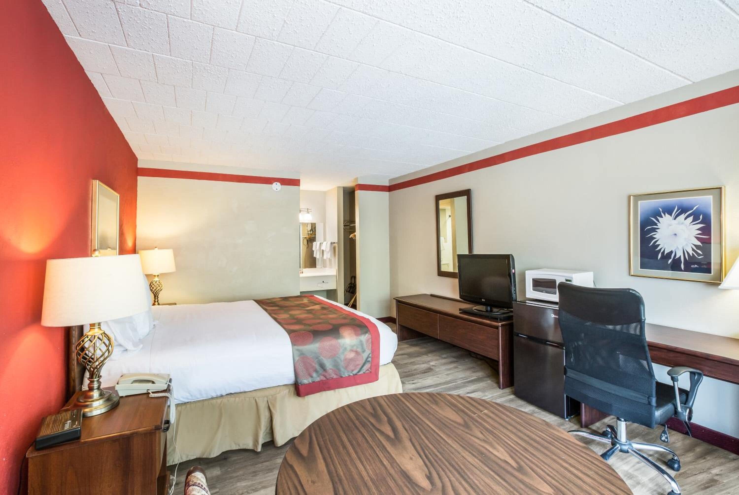 A hotel room with a bed, desk, chair, TV, and a microwave.